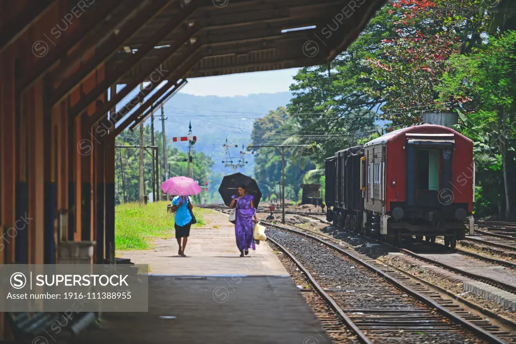 Two women with umbrellas walking in train station platform, Sri Lanka