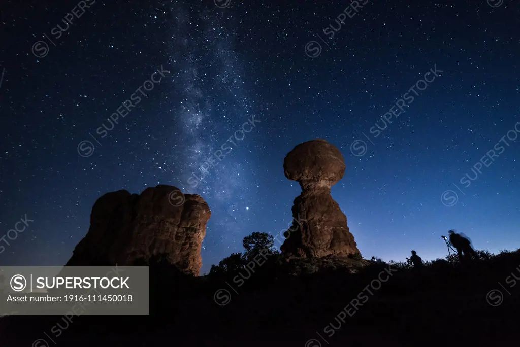 Photographers at dusk taking pictures to the Milky Way behind the Balanced Rock, Arches National Park, USA