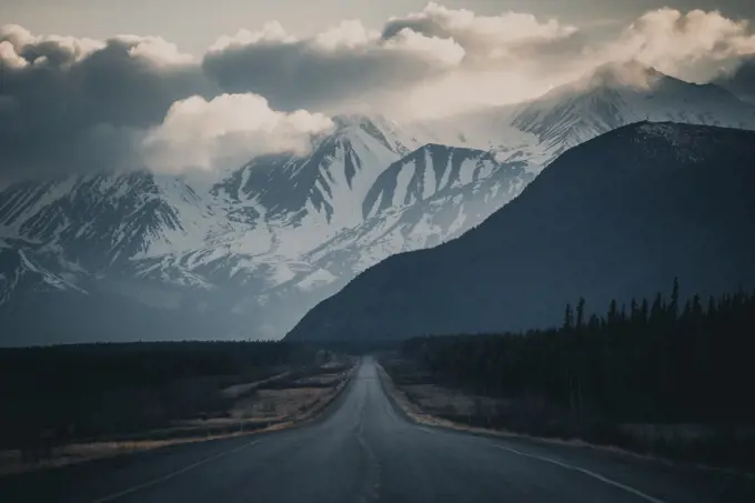 An endless road leads to the mountains, while storm clouds form in the sky. Yukon Territory, Canada