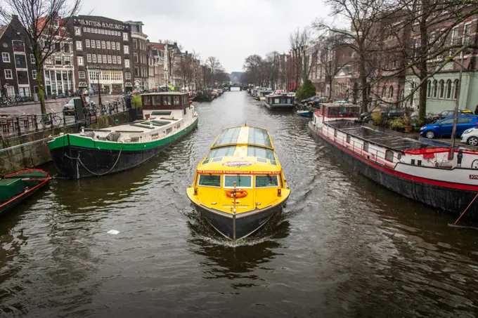 A bright yellow boat floats on the Amsterdam Canal in Amsterdam, Netherlands