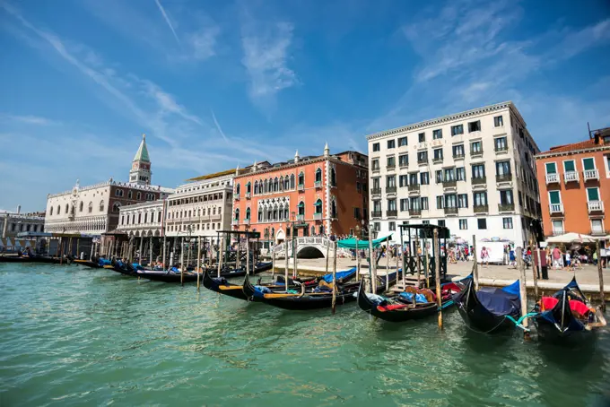 Gondolas attached to the main Venice road with people walking behind on a sunny day, Venice, Italy.