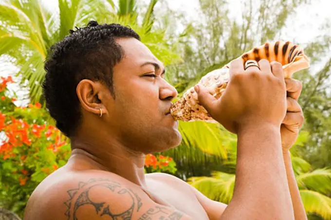 Tahiti, French Polynesia, Bora Bora, close-up of man blowing conch shell