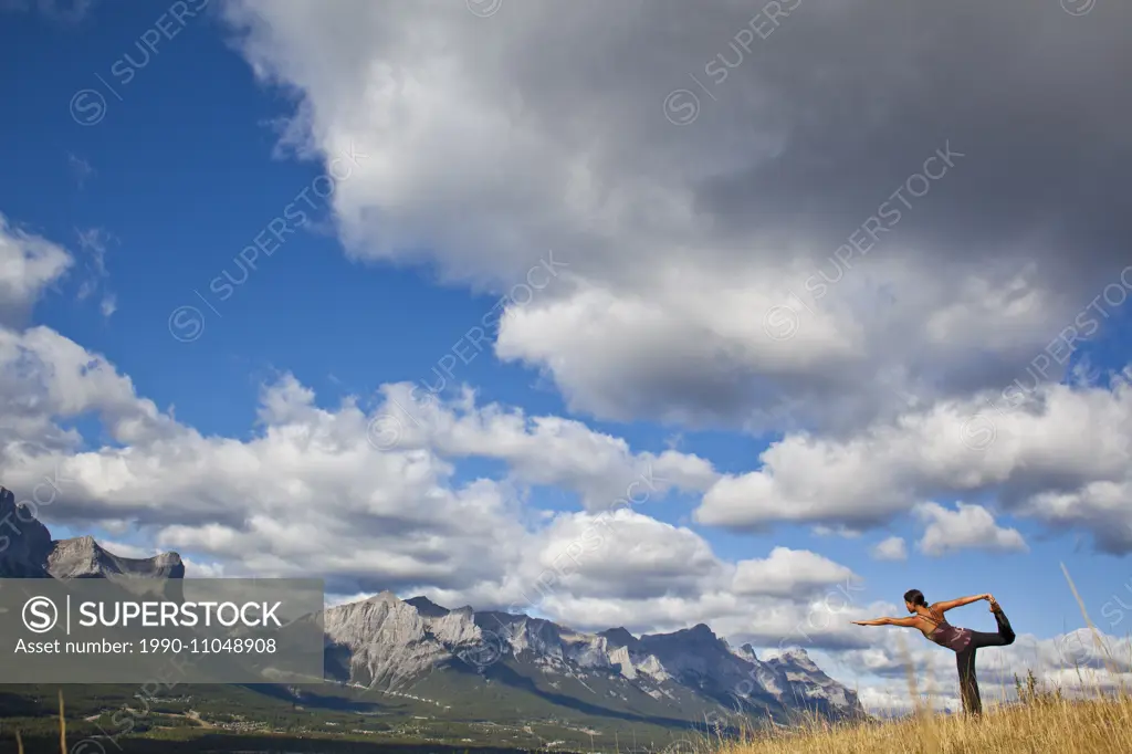 A young woman practicing yoga on a hill above the town of Canmore, AB