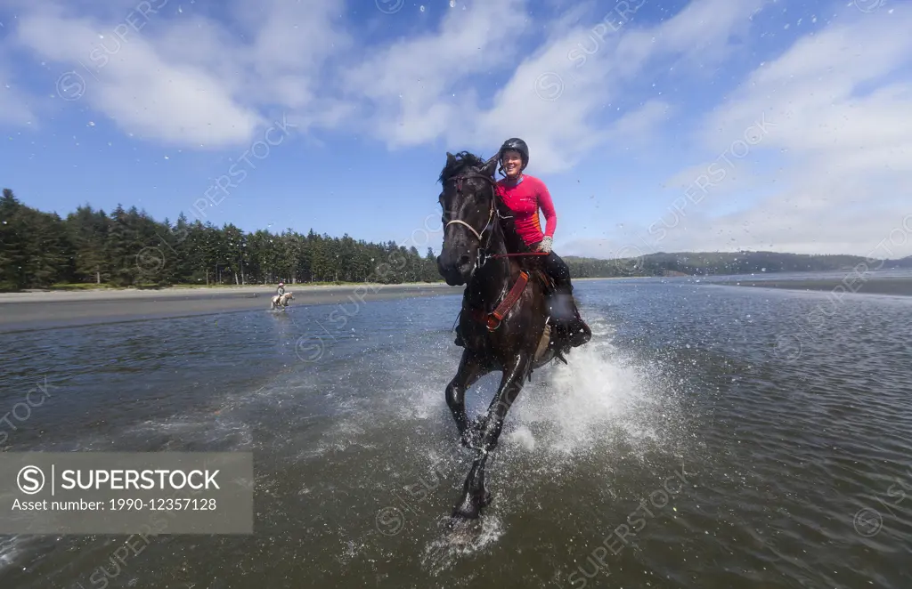 Horse enthusiasts run their horses in the low tidal waters on Stories Beach near Port Hardy.