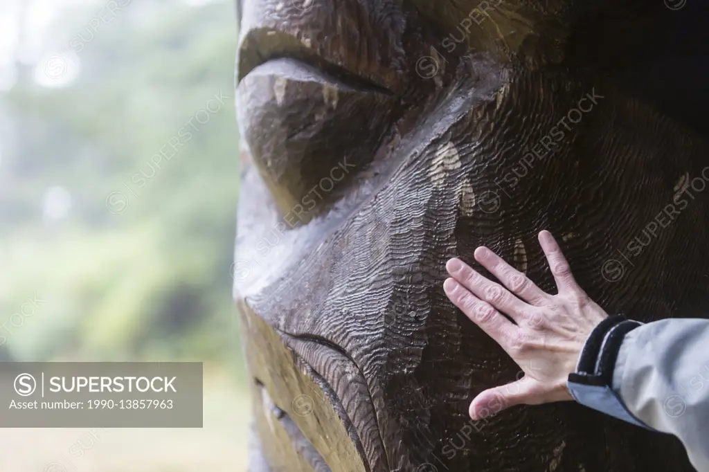 A wet memorial pole reveals its textural layers to a visitor at Friendly Cove, Yuquot, West Coast Vancouver Island, British Columbia, Canada