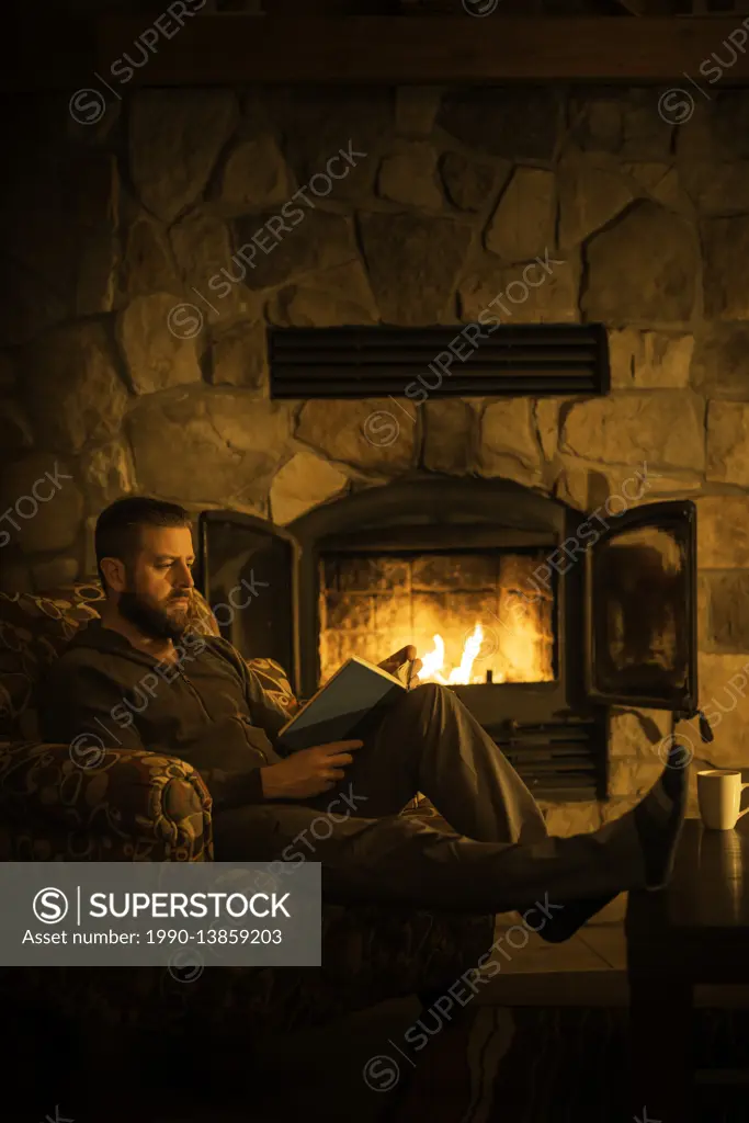 Man (40) sitting by a warm open fire at a log cabin ski chalet in Mont Tremblant, Quebec, Canada