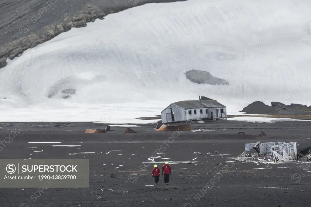 Two adventure tourists walk along the volcanic landscape and deteriating buildings of Deception Island, South Shetland Islands