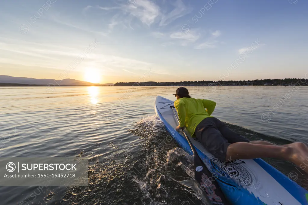 A stand up paddleboarder launches his board into the evening waters of Comox Bay, The Comox Valley, Vancouver Island, British Columbia, Canada