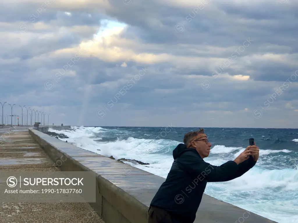 Tourist photographing waves on Malecon, Havana, Cuba