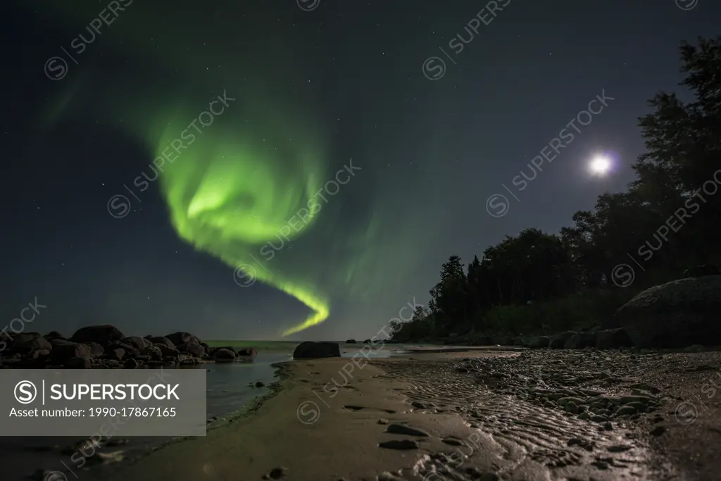 Aurora dancing over water under a full moon in Lake Winnipeg, Manitoba Canada