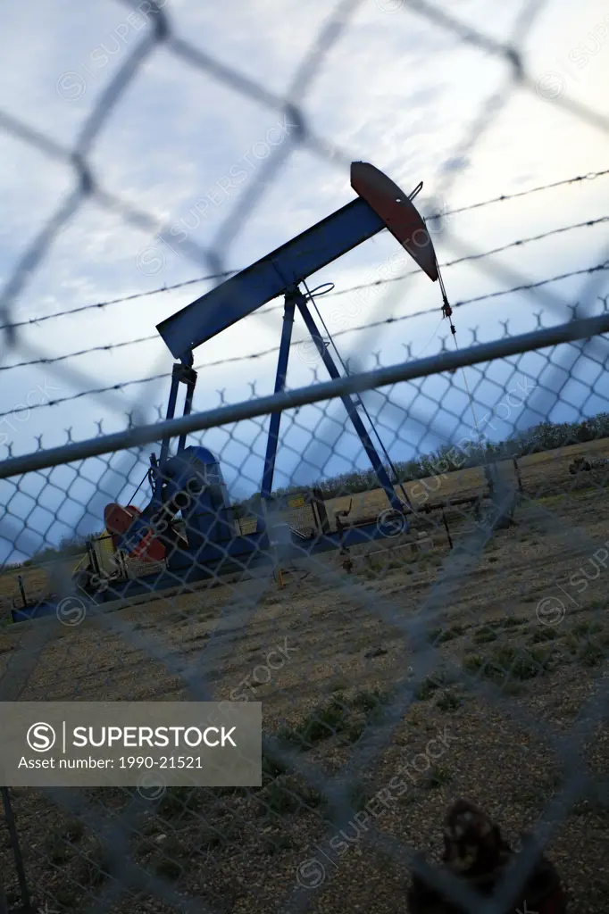 Pump jack behind chain link fence at dusk.