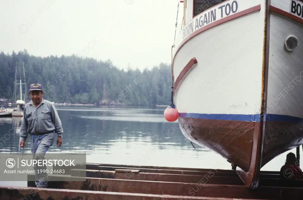 Kyuquot, first nations fisher examines boat hull, Vancouver Island, British Columbia, Canada