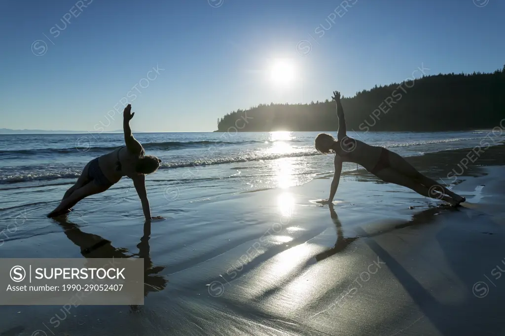 Two friends practice yoga poses on China Beach along the Juan De Fuca Trail.  Southern Vancouver Island, British Columbia, Canada