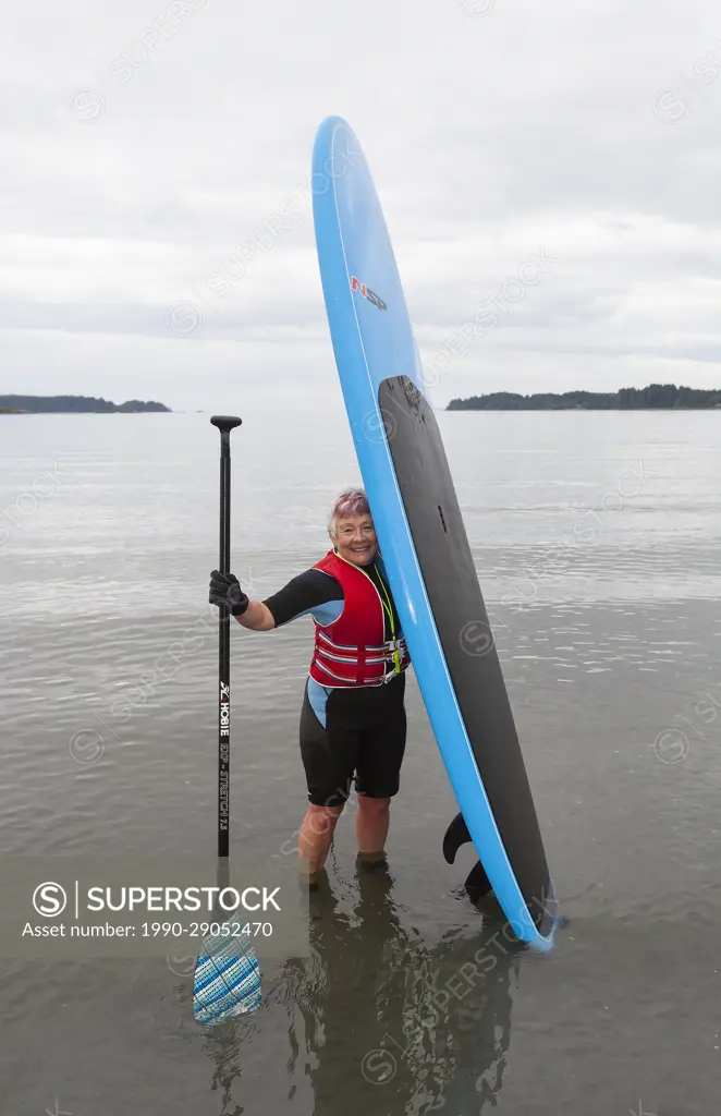 A senior woman comes ashore with her stand up paddle board after paddling in the waters off of Stories Beach near Port Hardy