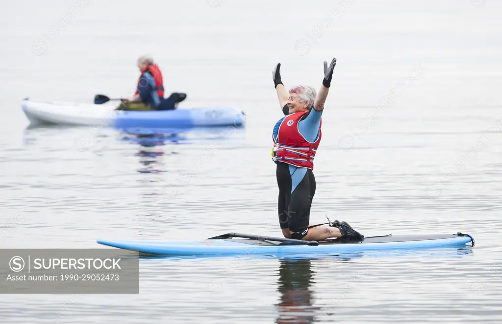 A senior woman stretches while paddle boarding at Stories Beach near Port Hardy.