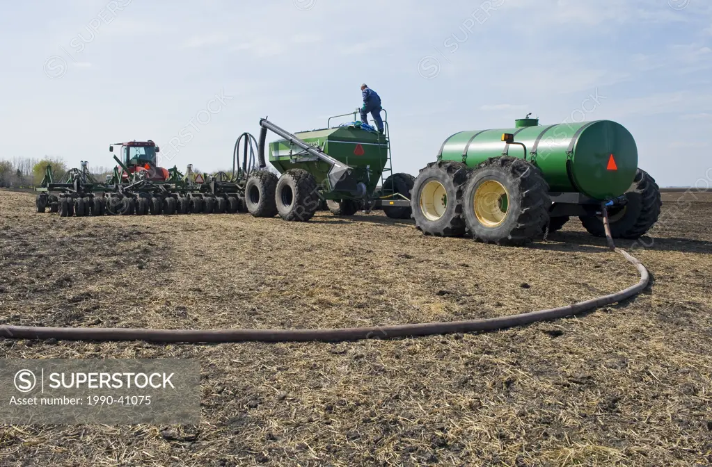 a farmer loads a seeder tank with canola seed and another tank with liquid fertilizer, near Dugald, Manitoba, Canada