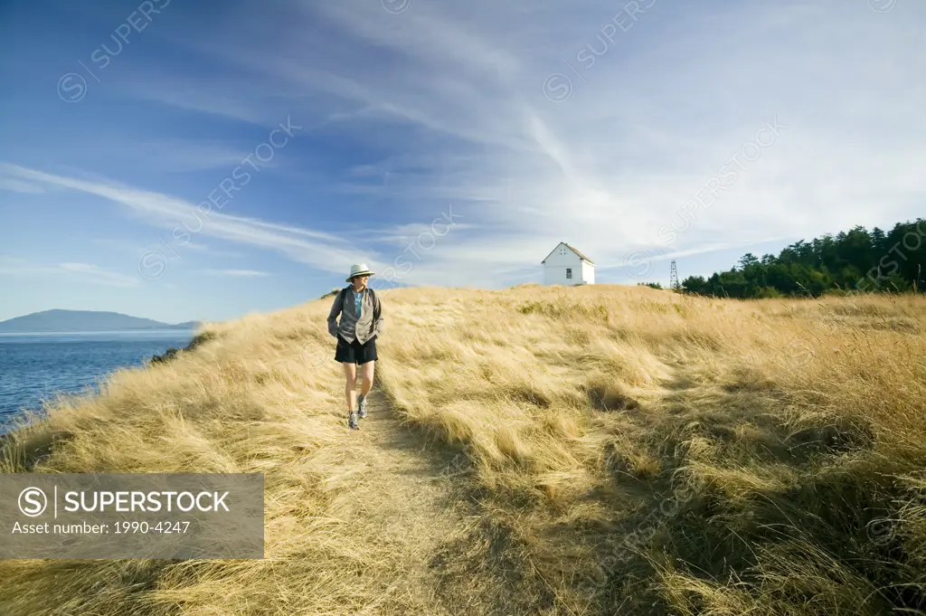 woman walking past old fog horn building at East Point Park and lighthouse, Saturna Island, British Columbia, Canada