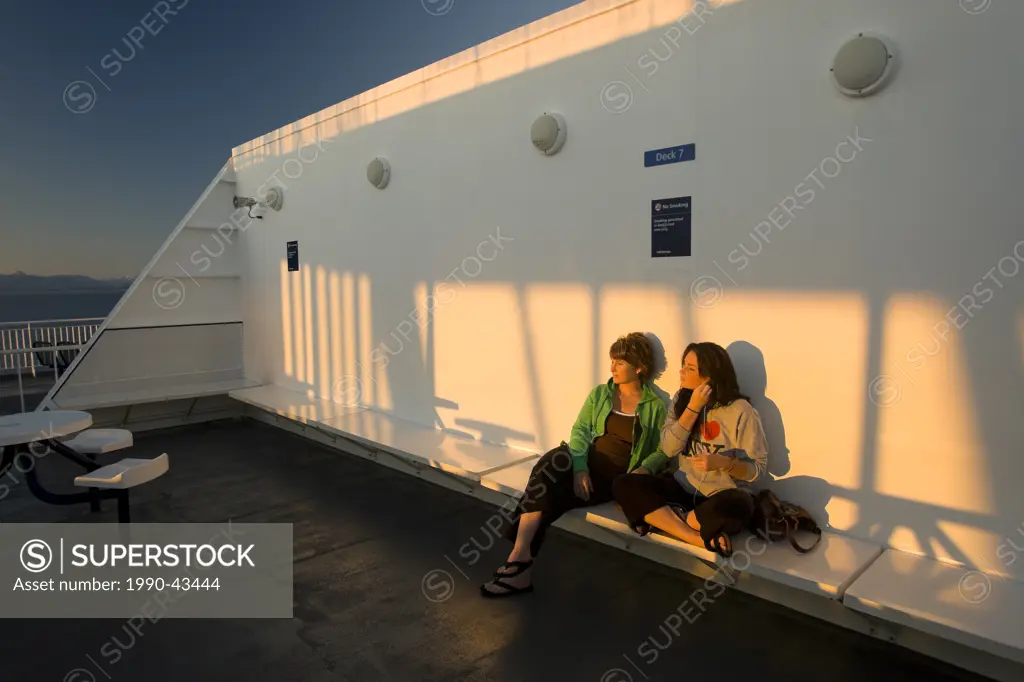 Mother and Daughter share a moment together alongside the setting sun while aboard BC Ferry bound for Vancouver. Vancouver, British Columbia, Canada