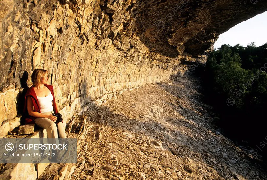 A hiker rests along the Bruce Trail at Overhanging Point, a large karst rock formation, in Bruce Peninsula National Park, Ontario, Canada