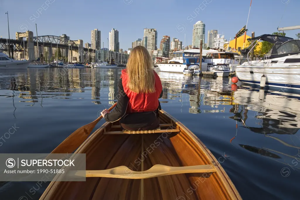 Girl paddling canoe in False Creek off Granville Island, Burrard Bridge and downtown condominiums in background, Vancouver, British Columbia, Canada.