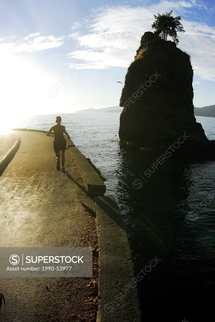 Woman enjoys a sunny day running on the Stanley Park Seawall, Near Siwash Rock, Vancouver, British Columbia, Canada.