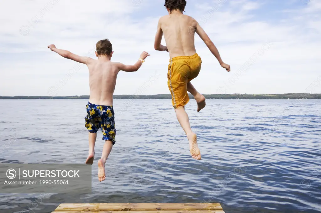 two boys 9 & 12 years old jumping off dock into lake, Sylvan Lake, Alberta, Canada.