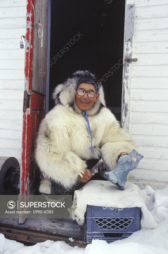 Inuit elder works on soapstone carving in traditional clothing, Kimmirut, Baffin Island, Nunavut, Canada