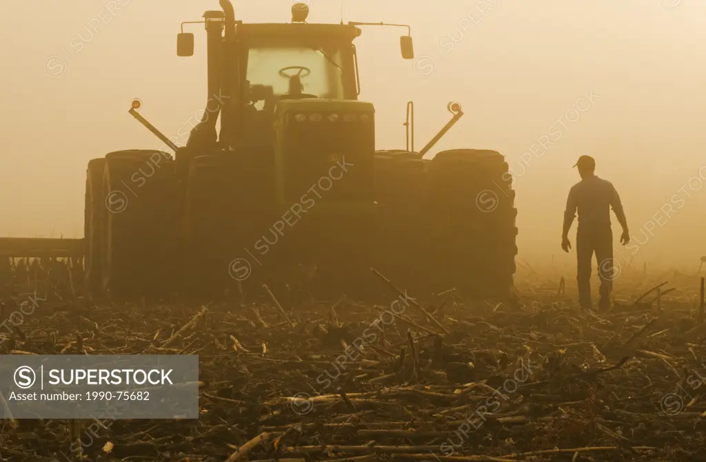 a farmer walks toward a tractor pulling cultivating equipment in a sunflower stubble field, near Lorette, Manitoba, Canada