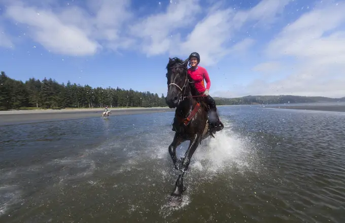 Horse enthusiasts run their horses in the low tidal waters on Stories Beach near Port Hardy.