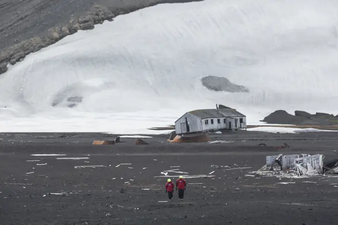 Two adventure tourists walk along the volcanic landscape and deteriating buildings of Deception Island, South Shetland Islands