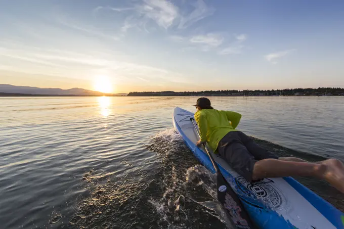 A stand up paddleboarder launches his board into the evening waters of Comox Bay, The Comox Valley, Vancouver Island, British Columbia, Canada