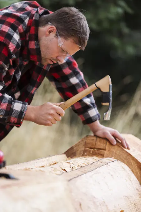 A young First Nations carver uses his adze to form out a design element on a totem pole, Comox, The Comox Valley, Vancouver Island, British Columbia, ...