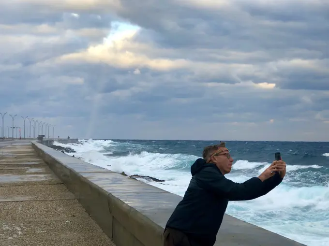 Tourist photographing waves on Malecon, Havana, Cuba