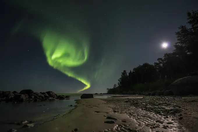 Aurora dancing over water under a full moon in Lake Winnipeg, Manitoba Canada