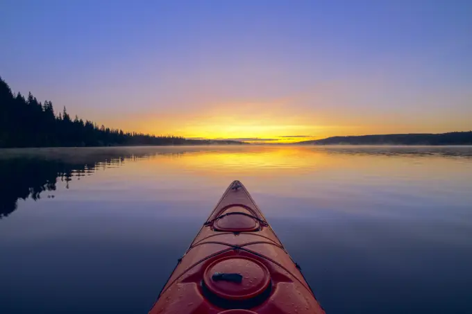 Kayaker with red kayak on Beaver Lake at sunrise, Lake Country, British Columbia, Canada.