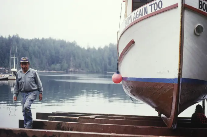 Kyuquot, first nations fisher examines boat hull, Vancouver Island, British Columbia, Canada