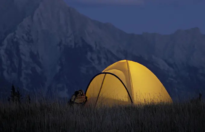 Glowing yellow tent at camp in mountains at dusk.