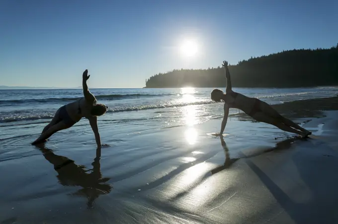 Two friends practice yoga poses on China Beach along the Juan De Fuca Trail.  Southern Vancouver Island, British Columbia, Canada