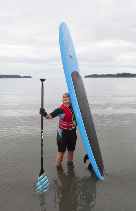 A senior woman comes ashore with her stand up paddle board after paddling in the waters off of Stories Beach near Port Hardy