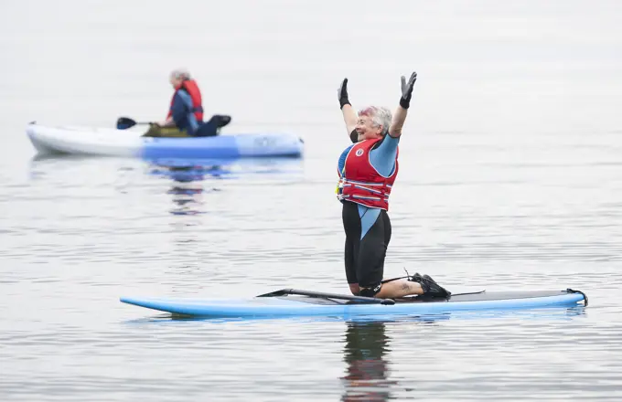 A senior woman stretches while paddle boarding at Stories Beach near Port Hardy.