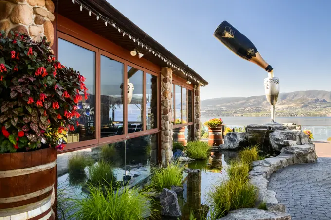 A bottle of sparkling wine, seemingly suspended in air, pouring wine into a glass on the patio at the Summerhill Pyramid Winery in Kelowna, British Columbia.