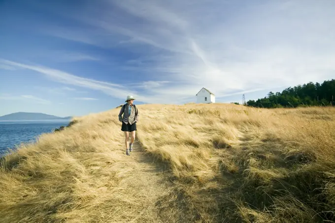 woman walking past old fog horn building at East Point Park and lighthouse, Saturna Island, British Columbia, Canada