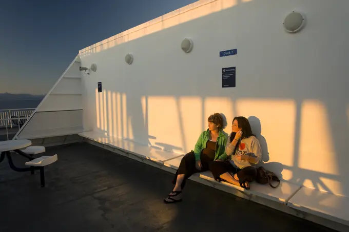 Mother and Daughter share a moment together alongside the setting sun while aboard BC Ferry bound for Vancouver. Vancouver, British Columbia, Canada