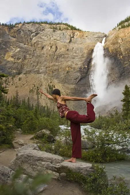 Young woman practicing yoga beneath Takakkaw Falls in Yoho National Park, Field, British Columbia, Canada