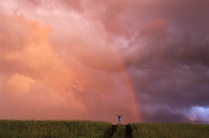 Girl on hill with arms outstretched, in front of rainbow, near Winnipeg, Manitoba, Canada.