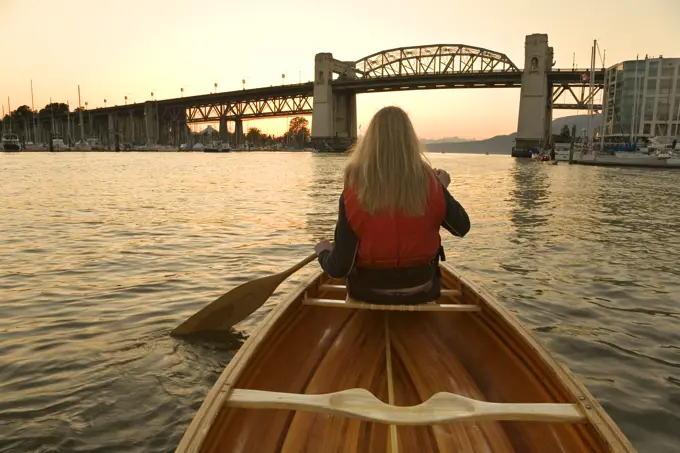 Girl canoeing in False Creek, Burrard Bridge at sunset, Vancouver, British Columbia, Canada.