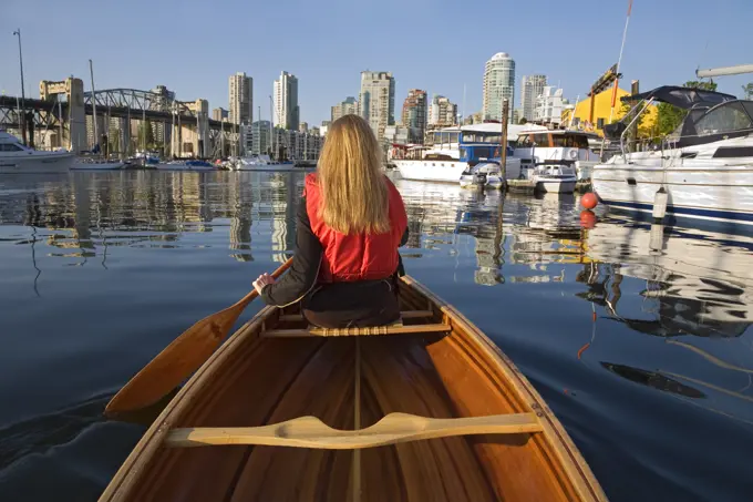 Girl paddling canoe in False Creek off Granville Island, Burrard Bridge and downtown condominiums in background, Vancouver, British Columbia, Canada.