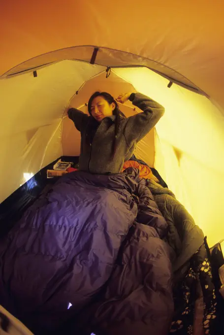 A young woman waking and stretching in a tent in Jasper, Alberta, Canada.