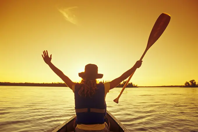Female canoeist, arms raised welcoming the sunset, Otter Falls, Whiteshell Provincial Park, Manitoba, Canada