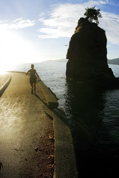 Woman enjoys a sunny day running on the Stanley Park Seawall, Near Siwash Rock, Vancouver, British Columbia, Canada.